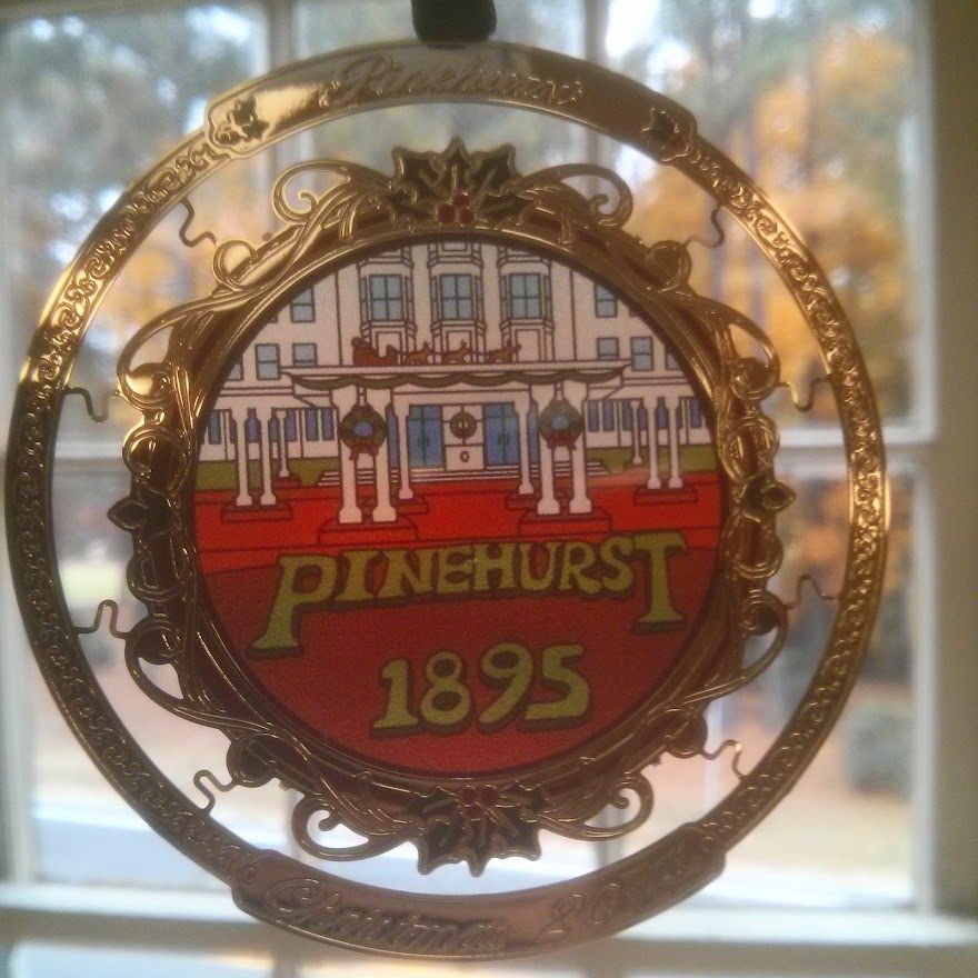 Brass Pinehurst ornament with a painted clubhouse centre, hanging in a window.